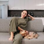 A woman relaxing with her Yorkshire Terrier on a cozy sofa in a modern kitchen setting.